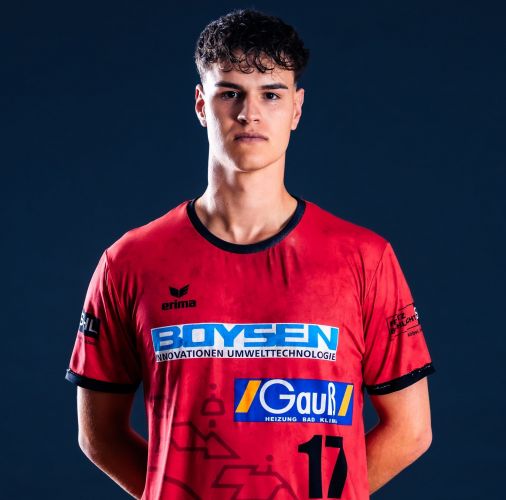 Junger Mann im roten Sporttrikot mit den Nummern 17, vor dunkelblauem Hintergrund, frontal stehend.